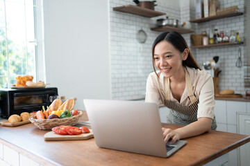 Adorable woman using laptop for recipe while preparing food in kitchen.