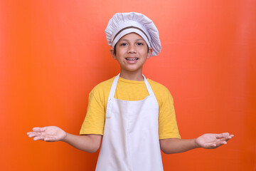 Cute boy wearing chef uniform welcoming guest isolated on orange background. Food and cooking...