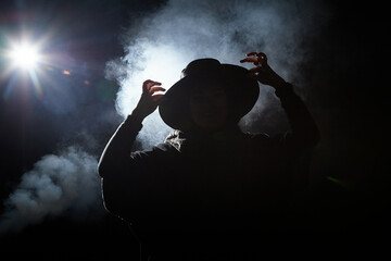 Silhouette or shadow of a woman in black warm coat and black hat on dark background with smoke....