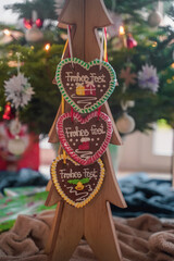 Colorful Christmas handmade gingerbread in the shape of a heart hangs on a wooden tree close-up. Christmas decor and food. Christmas cozy atmosphere. Festive fair. Selective focus