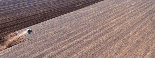 A tractor in the field cultivates the soil before the start of the sowing campaign. Drone view.