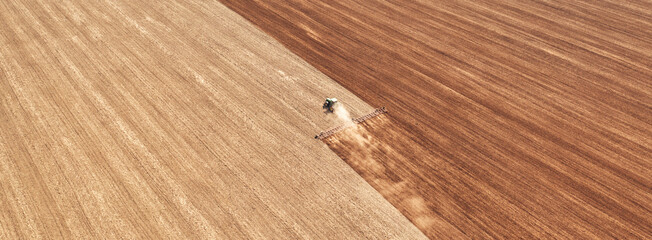 Fototapeta premium A tractor in the field cultivates the soil before the start of the sowing campaign. Drone view.
