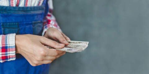 woman counts banknotes from bundle of money of 50 dollars on gray and blue background. woman worker is holding dollar bills in her hands. Closeup view.