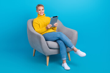 Full body size photo of blonde short hair business lady wear yellow knitted jumper hold apple tablet sit armchair isolated on blue color background