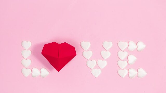 4k Red origami heart appears on a pink background. From white small hearts the word Love appears. Greeting card. Concept of valentine's, mother's day holiday, wedding and other. Stop motion animation.