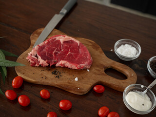 Composition of raw steak meat on a kitchen wooden table with spices, salt, vegetables and herbs, cooking, top view, copy place for recipes.