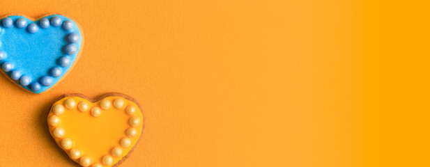 Two cookies in shape of hearts decorated by yellow and blue icing and sprinkles on yellow background