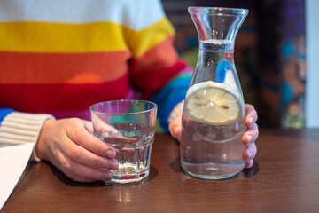 Women's hands hold a carafe of water and lemon next to a glass glass. Sweater with LGBT flag