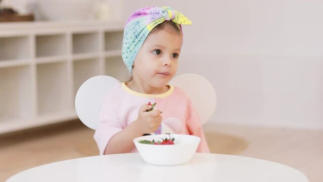 Happy child at the table eats strawberries at home. Concept of healthy eating.