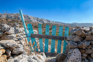 a view of amorgos island, cyclades, greece. A blue wooden gate leading to a meadow