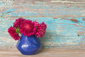 Bouquet of purple asters flowers in blue vase on old blue paint wooden background; copy space