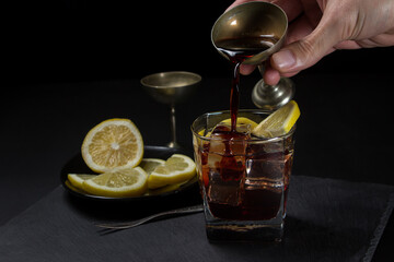 Preparation of a cocktail on a black background. Hand adding syrup to glass with ice