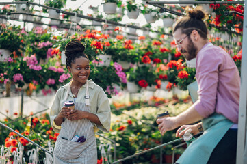 Fototapeta na wymiar Multiracial florists working in a green house plant nursery and drinking coffee