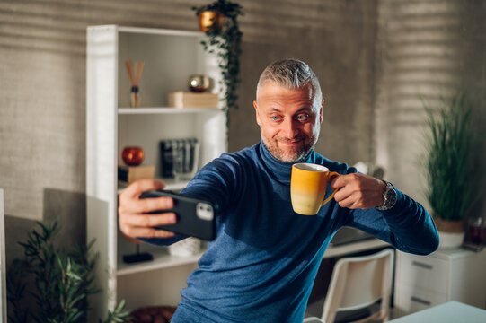 Middle Aged Man Taking Selfie With A Smartphone And Drinking Coffee At Home