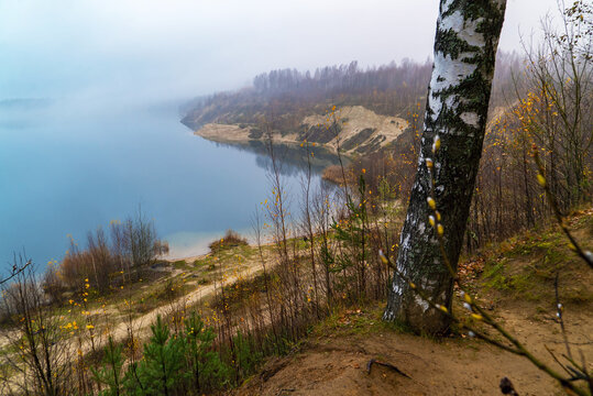 Fog descends on the lake on the steep shore .