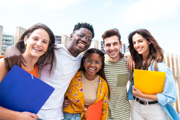 multiethnic group of cheerful students standing together outdoors with folders looking at camera -...
