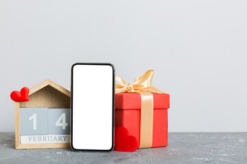 mobile phone with blank screen on colored background with hearts, calendar and gift box, valentine day 14 february concept perspertive view flat lay