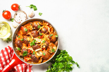 Meatballs with mushrooms in tomato sauce in a frying pan at light stone table. Top view with copy space.