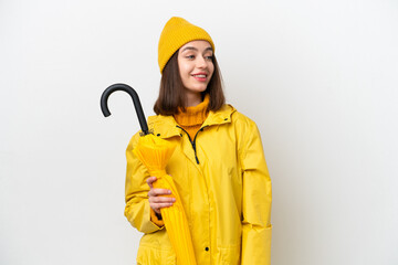 Young Ukrainian woman with rainproof coat and umbrella isolated on white background looking to the side and smiling