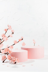 Naklejka premium Pink sakura flowers on branch with two cylinder podiums mockup in soft light, white interior on table in floral spring style for presentation cosmetic products, goods, branding, copy space, vertical.
