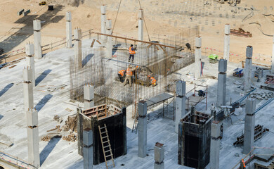 The construction of a monolithic-frame building, a team of builders sets in place a section of metal reinforcement filed by a crane. Slinger at work. Formwork elements.