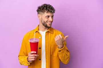 Fototapeta premium Young blonde man holding soda isolated on purple background pointing to the side to present a product