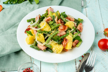 Delicious Belgian potato salad with green beans, bacon, ham. Traditional local european salad in a white round plate on a wooden background.