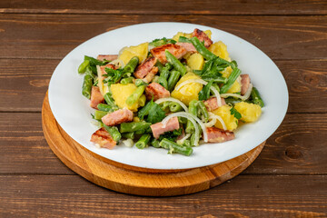 Liege potato salad is a traditional European dish in a white plate on a wooden table. salade liegeoise