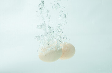 Two eggs fall into clear water, bubbles and splashes.