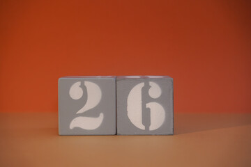 Number 26 on wooden grey cubes close-up. Concept of date time. Math concept. Copy space for text or event. White numbers 26 on building blocks, orange background