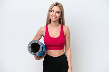 Young sport blonde woman going to yoga classes while holding a mat isolated on white background thinking an idea while looking up