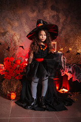 Little girl in a witch's hat and black dress on the background of the cobwebs. Image for Halloween. Halloween costume