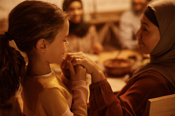 Middle Eastern granddaughter holding grandmother's hand during family dinner at dining table.