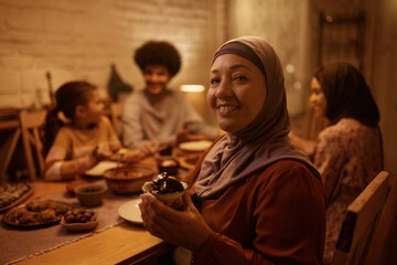Happy mature Muslim woman holding dates during family meal and looking at camera.