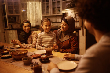 Happy Muslim multigeneration family talking during dinner at dining table.