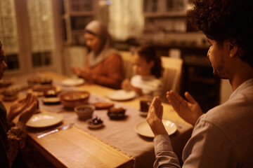 Close up of Middle Eastern man prays with his family during dinner at dining table.