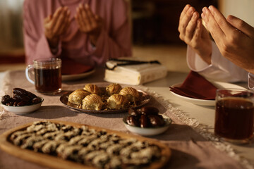 Traditional Muslim desserts at dining table with couple praying in background.