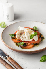 Caprese salad in modern feed with tomatoes, basil, mozzarella, pesto. Traditional Italian food with cutlery on white background, menu