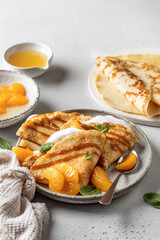 Crepes with fresh mandarin, caramel, cream in the filling and mint leaves on white textured background. Maslenitsa or Pancake week traditional concept, text space