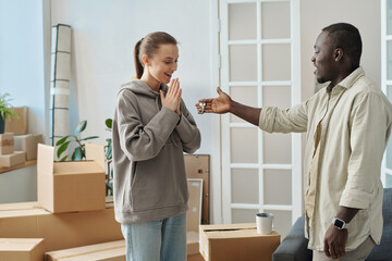 Happy girl getting keys from her new apartment from real estate agent, they standing in the room among packed boxes