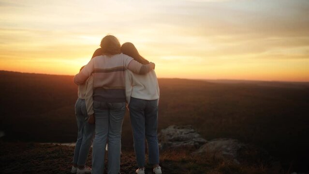 Mother and Daughters enjoying the view after a mountain hike during sunset. A mother hugs her daughters