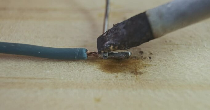 Soldering iron melts the tin wire to tin the copper wire. Close-up, macro. Preparing the wire for soldering.