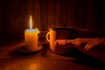 A hand grabbing a cup by a candle during a power outage.