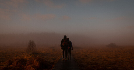 Fototapeta na wymiar People walking on a wooden path in a sunrise in the fog in Belgium.