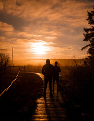 Fototapeta na wymiar People walking on a wooden path in a sunrise in the fog in Belgium