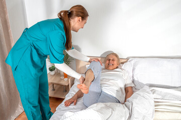 Nurse kinesiologist physiotherapist stretching, and masseuring leg of elderly woman at her home....