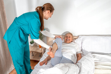 Obraz premium Nurse kinesiologist physiotherapist stretching, and masseuring leg of elderly woman at her home. Solicitous professional medical female staff caring for senior patient. Lifestyle, nursing service