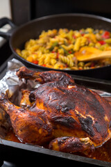 Whole chicken baked in sauce on foil in the background a frying pan with pasta.