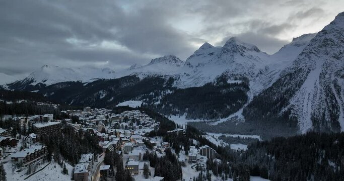 Aerial Shot above a snowy Swiss Ski town and mountains at dawn