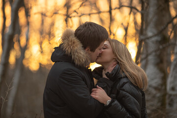 Loving young couple of woman and man laughing together walking in the snow forest, hugging and kissing. Valentine's day surprise adventure trip to mountains for weekend just in two